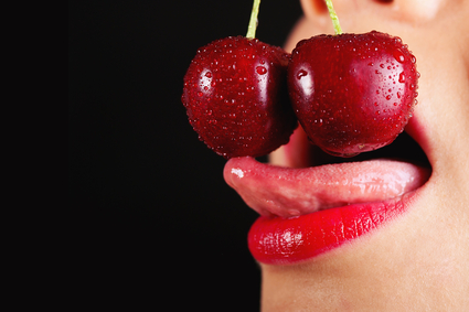 Detail of  young woman mouth with cherries against black backgro